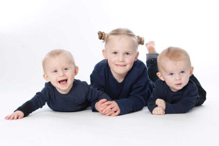 geschwisterportrait im studio, klassisch vor weiß, zwillinge mit schwester liegen auf dem bauch und lachen