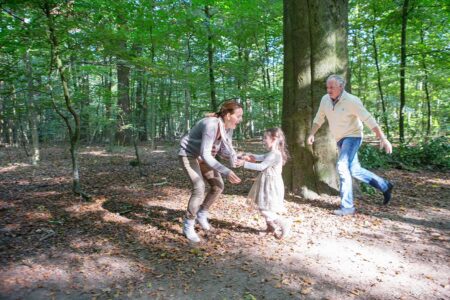 eltern und kind spielen fangen im wald, ein bewegtes familienfoto