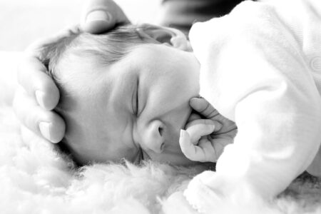 neugeborenes mit hand vom papa am kopf in scharz-weiß, auf lammfelll liegend