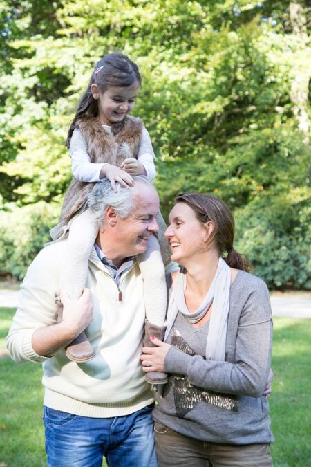 lachendes familienbild im stadtpark mit tochter auf den schultern des vaters