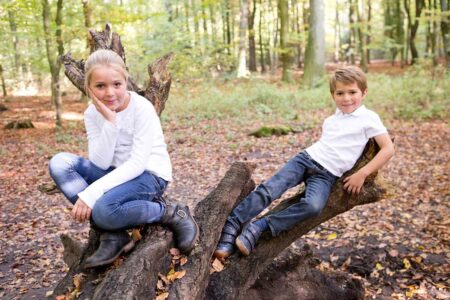 junge und mädchen sitzen im wald auf einem baumstamm und schauen entspannt und lässig in die kamera