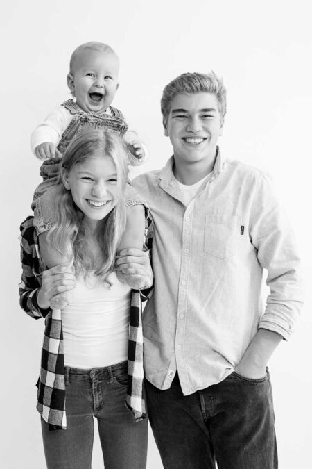 teenagergeschwister mit baby auf den schultern, lachendes portrait im studio