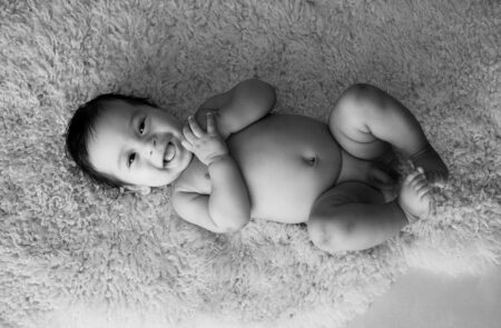 baby liegt lachend auf einem schaffell