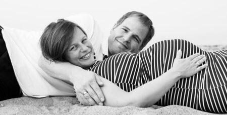babybauchfoto von liegendem und lächelnden pärchen am strand an der ostsee