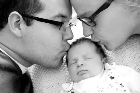 mama und papa küssen von zwei seiten ihr neugeborenes