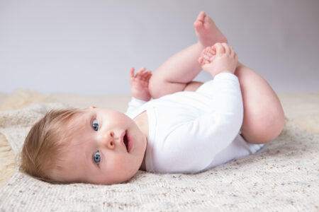 süßes baby liegt mit füsschen in der luft auf einer decke und schaut in die kamera