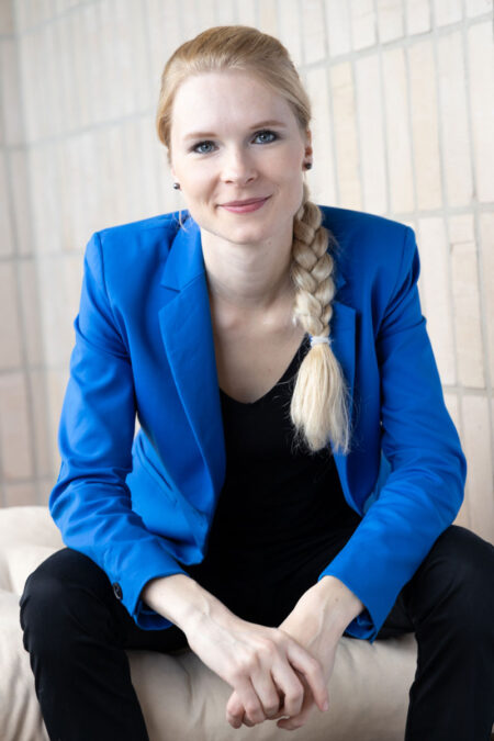 blonde frau mit zopf und blauem sacko lächelt in die kamera