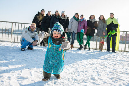 Kleinkind im Schneeanzug läuft von einer Gruppe weg auf die Kamera zu