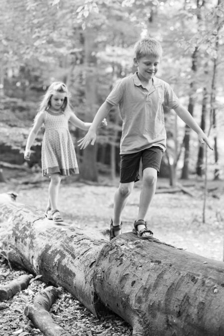 Junge und Mädchen balancieren im Wald auf einem Baumstumpf - ein natürliches Kinderportrait