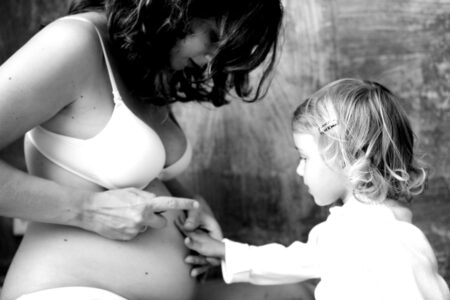 individuelles Babybauchfoto mit staunendem Geschwisterkind welches den Bauch anfasst