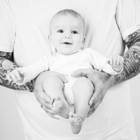 baby auf dem arm vor papas bauch, papa hat volltätowierte arme und das baby strahlt