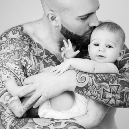 baby auf papas volltätowiertem arm, er küsst das baby