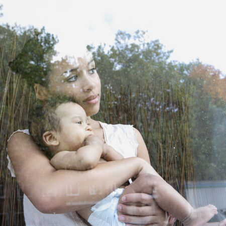 mama mit baby auf dem arm hinter einer fensterscheibe, ganz verträumt