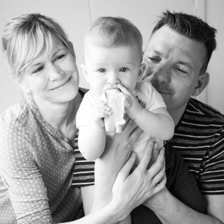 baby isst banane, im hintergrund stolze mama und papa