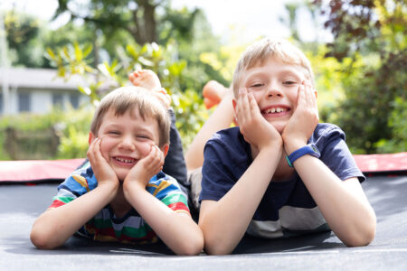 brüder schulkinder liegen auf trampolin im garten und lachen in die kamera