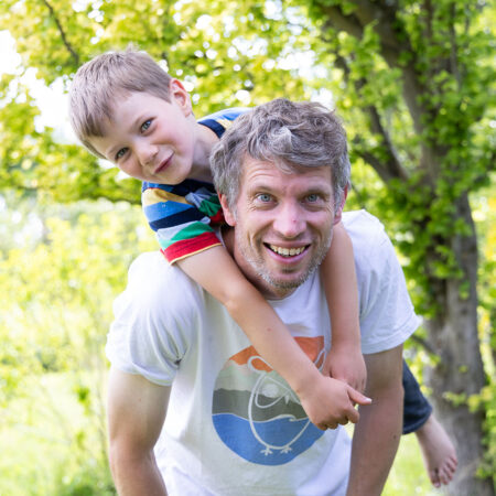 vater mit lachendem sohn auf den schultern im sommergarten