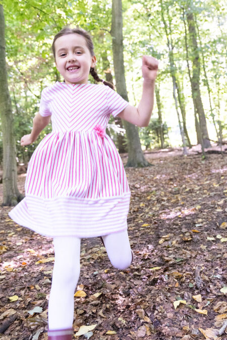 schulkind im rosa kleid läuft im ald übermütig auf die kamera zu