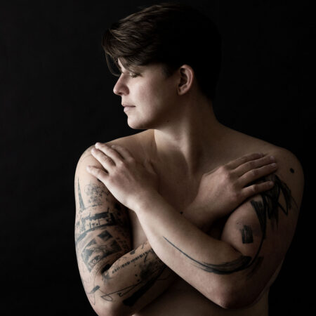 verschränkte arme vor dem oberkörper, tattoos auf den armen, aktfoto einer frau